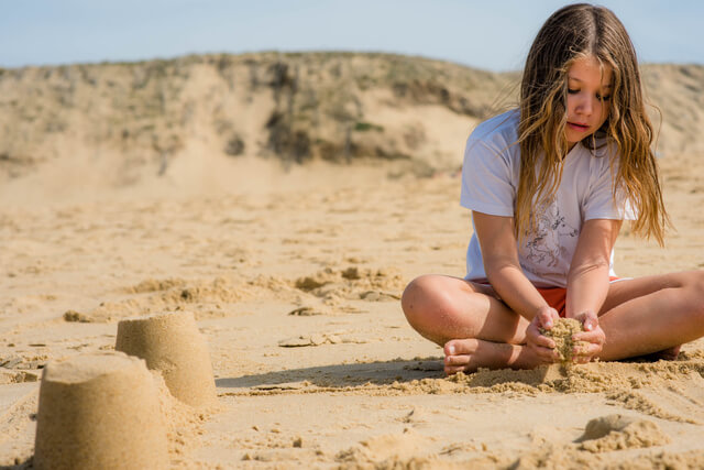 A little girl sat on the sand building sand castle