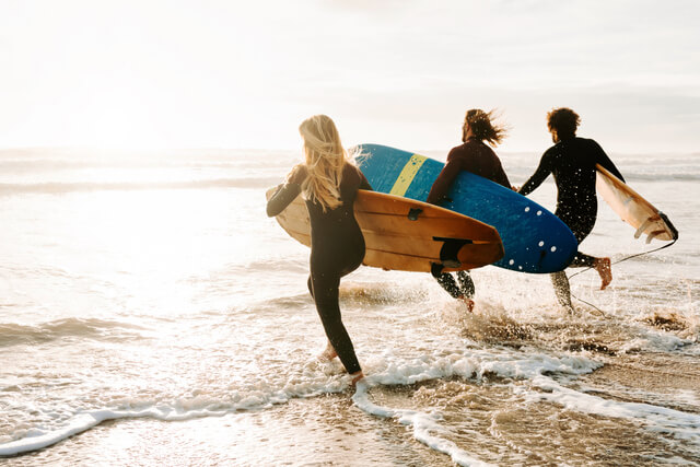 Three people running into the sea holding surf boards