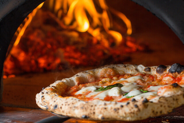 A cheese pizza cooking in a woodfired pizza oven