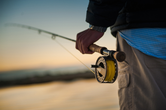 Man holding a fly fishing rod at sunrise