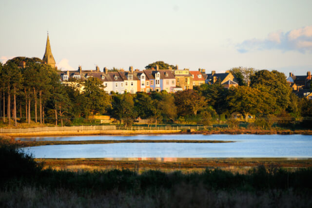 A view across a stetch of open water to the colourful houses of Alnmouth beyond