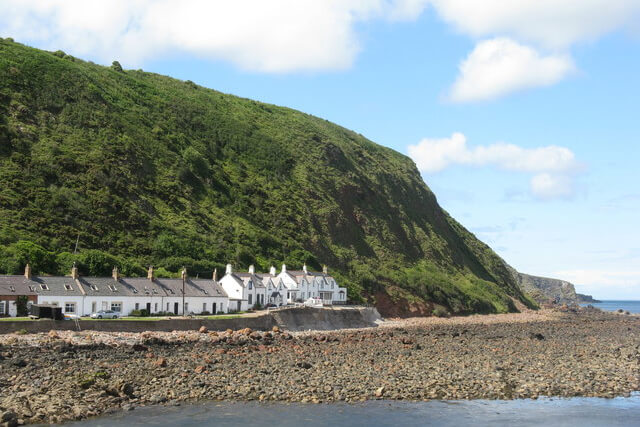 A view from the harbour of Burnmouth Beach a row of white houses and Burnmouth Hill sitting behind