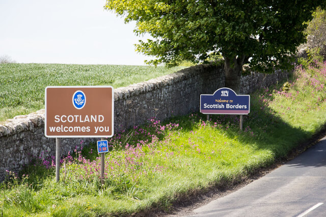 Two welcome signs on the left hand side of a road crossing the border into Scotland